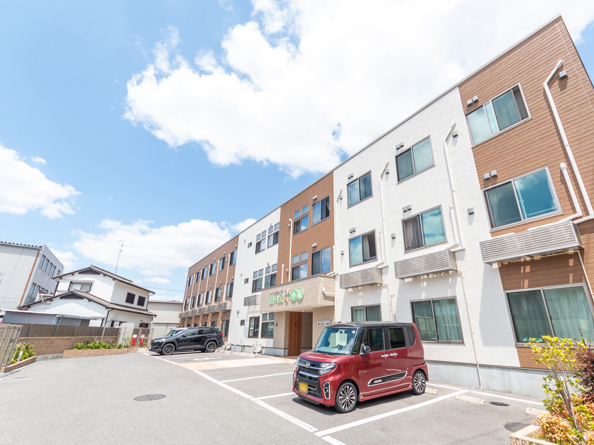 3階建ての建物はベージュとブラウンで玄関には住宅名が書かれた屋根もあり、駐車場も広い。