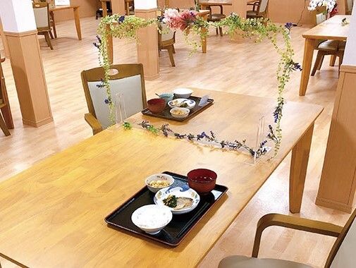飾りが付いたアクリル板が設置された木製のダイニングテーブル。アクリル板をはさんで2名分の食事が置かれている。