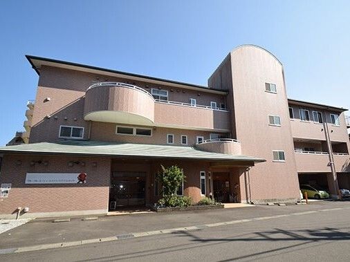 3階建ての建物はブラウン系で重厚感のある造り。各フロアにベランダがあり、玄関には車寄せが付き、広い駐車場がある。