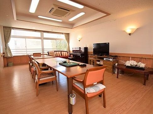 大型テレビやピアノが置かれ、季節の花が飾られたアットホームな雰囲気の共有リビング。中央には大きなダイニングテーブルが置かれている。