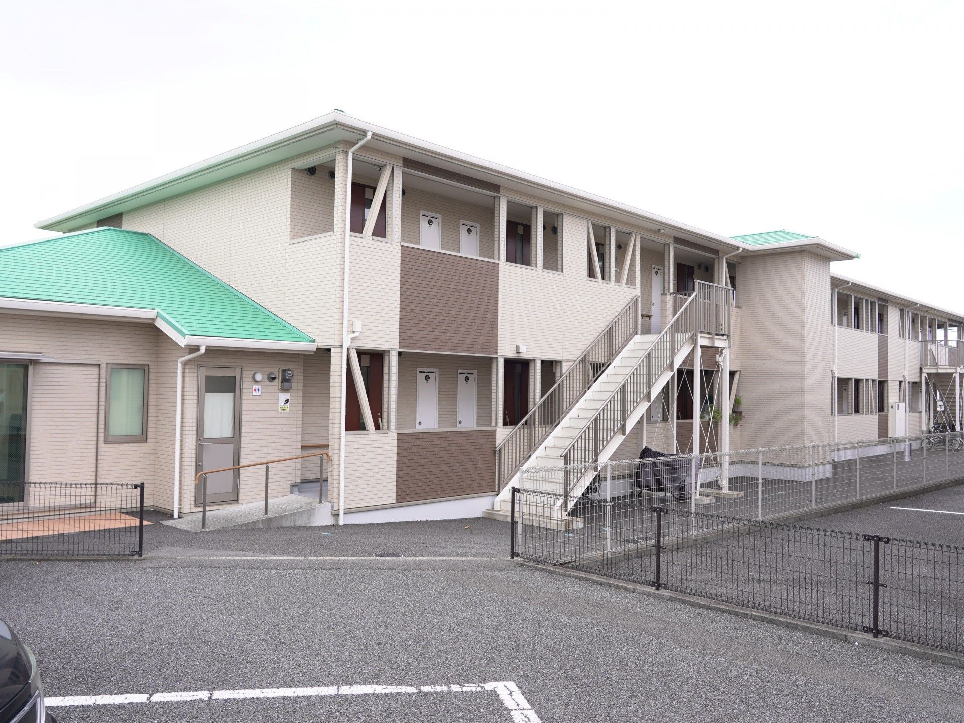屋外で高齢の夫婦が楽しそうに過ごしている様子。高齢女性は車いすを使っている。そばには男女の若いスタッフがいる。