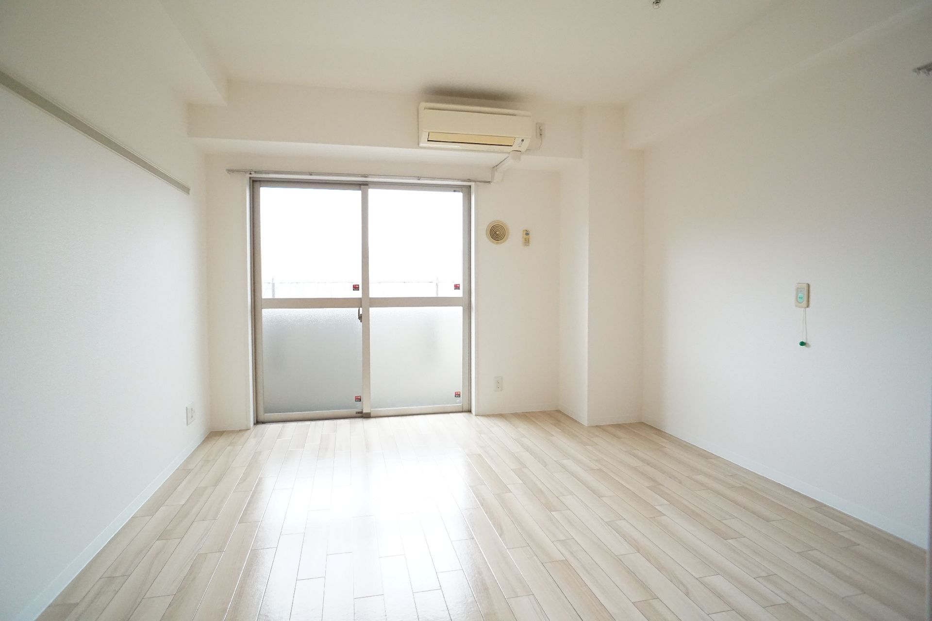窓とエアコンが付いた何も置かれていない白い部屋