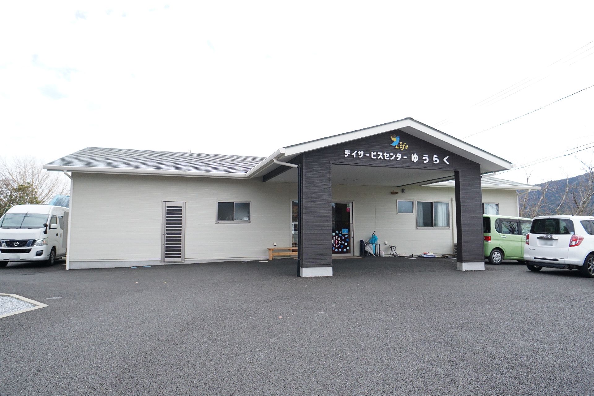 ブルーのエプロンを付けた若い女性スタッフに付き添われて原っぱのような場所を散歩している高齢女性。