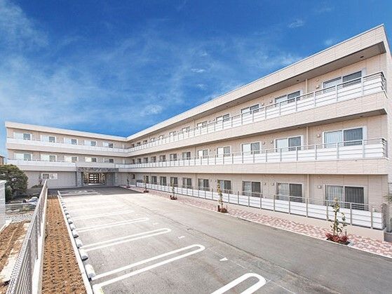 ベージュ系の外壁で敷地内には駐車場があり、各フロアにベランダが付いている。