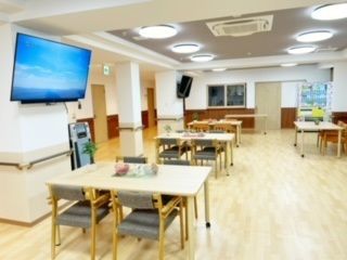 テーブルと椅子が多数置かれ、テレビが壁に掛けられているダイニング