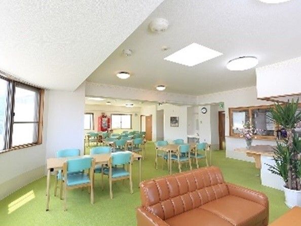 観葉植物や季節の花が飾られた共有スペースには複数のダイニングテーブルが置かれ、ブラウンのソファもある。