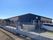 三角屋根が付いたダークグレーとブラウンの平屋建ての建物の周りには畑があり、敷地内には駐車場もある。