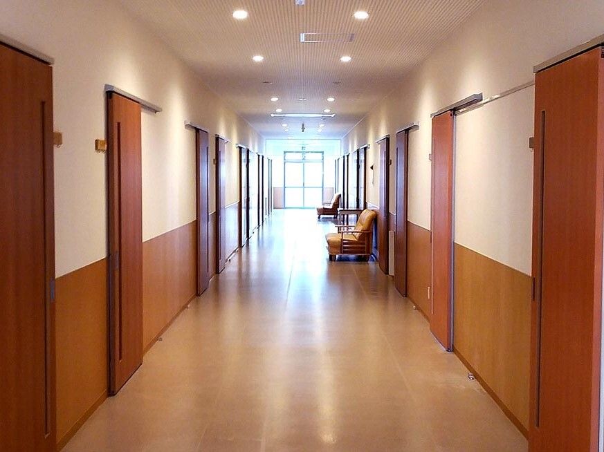 まっすぐな廊下の両サイドに居室のドアが並び、それぞれのドアのそばには小さな表札のようなプレートが貼られている。突き当りには大きなドアがある。