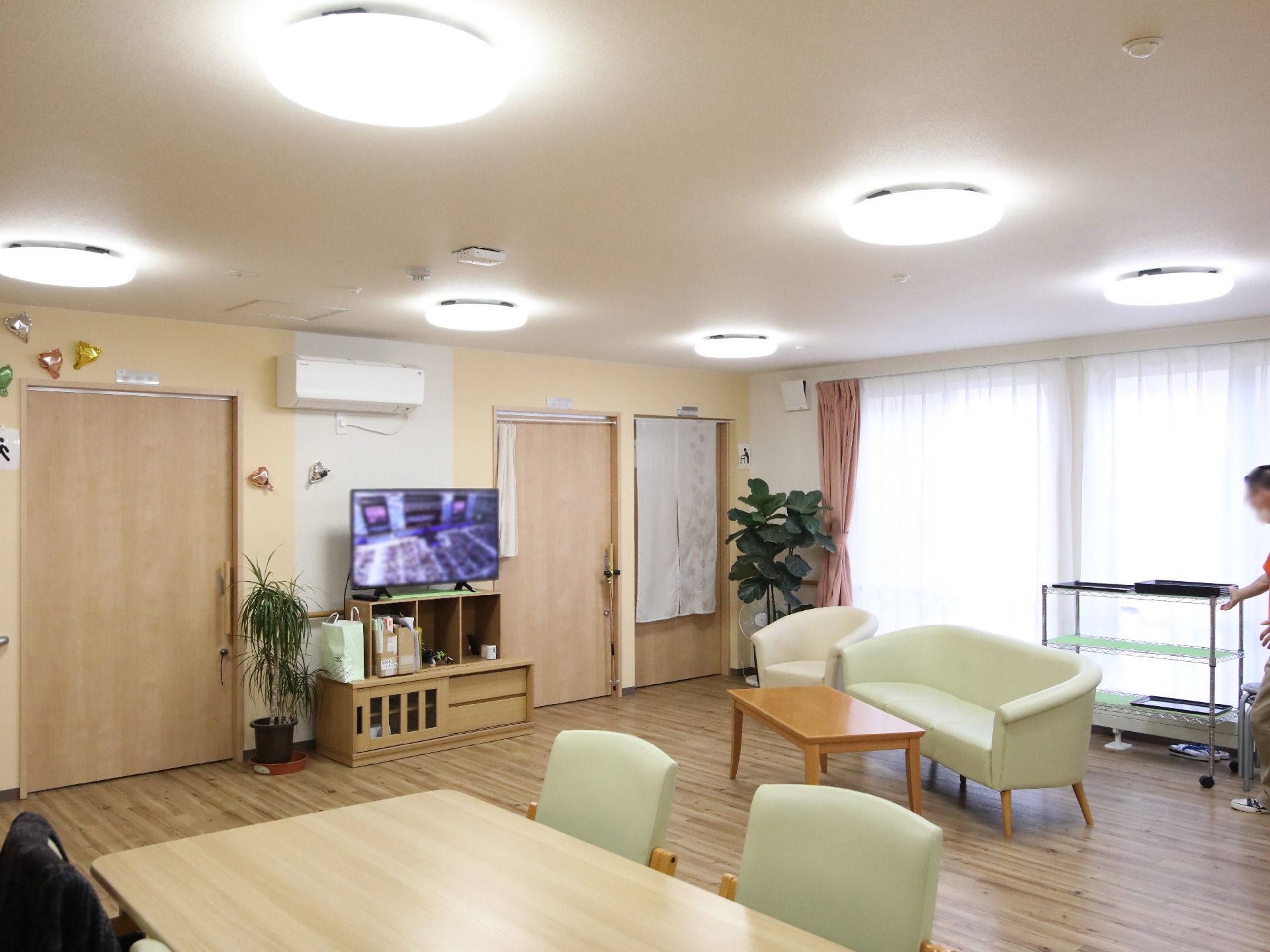 自然豊かな場所を車いすで散歩している高齢男性とそれを補助しながら話している女性スタッフ