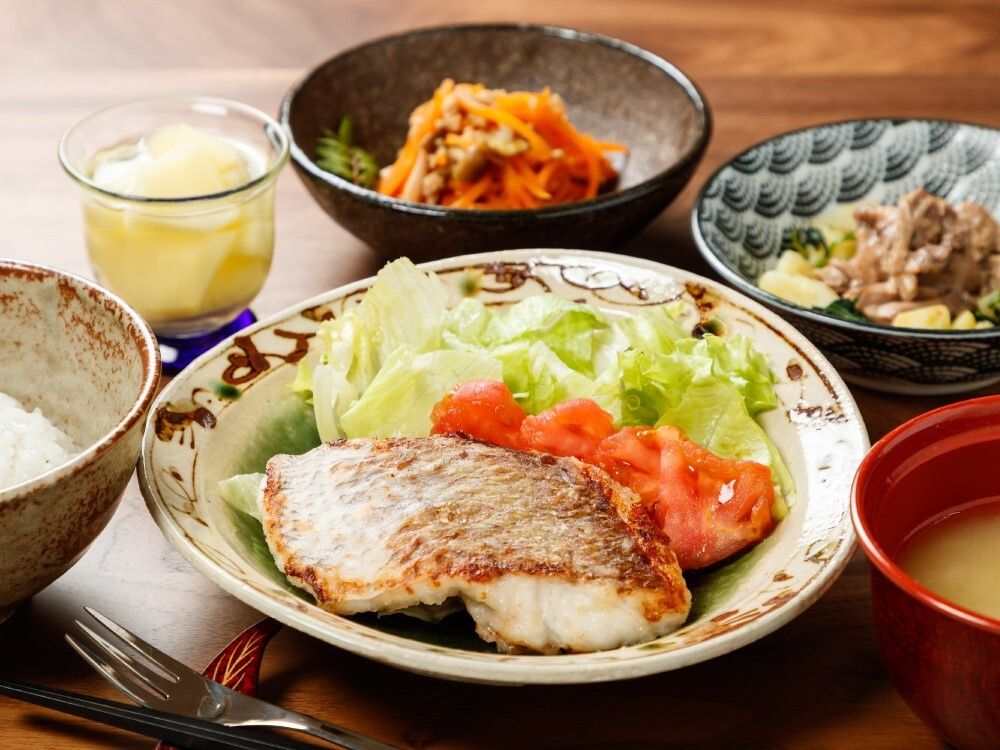 サラダが添えられた魚のグリルや白いご飯やみそ汁、野菜の料理が2品それぞれ異なる器に盛られている。