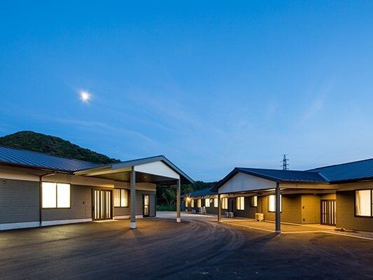 平屋建ての建物内には明かりが灯り、建物の外にあふれている。施設の建物の後ろには山の影が見える。他には特になにもない。