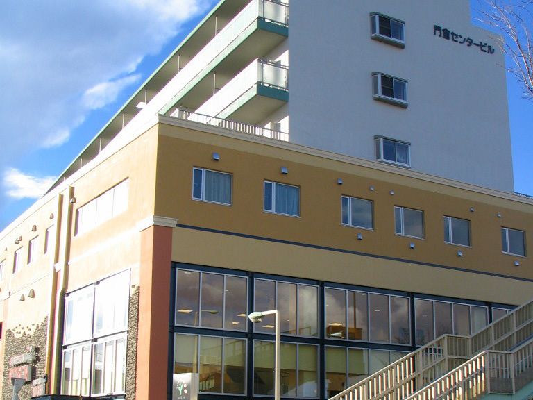 グレーの屋根が付いた2階建ての建物の周りには草木があり、緑が多い環境。玄関には車寄せが付き、ゆるやかなスロープが付いている。