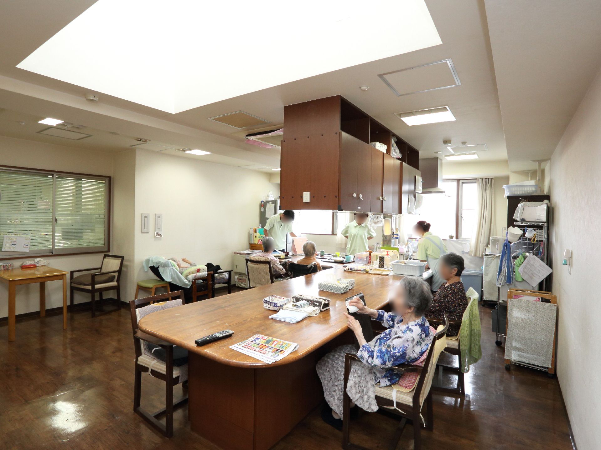 数名の入居者様とスタッフがおり、入居者様はイスに座りながら色々な作業をしている。スタッフはその入居者様の世話をしている。