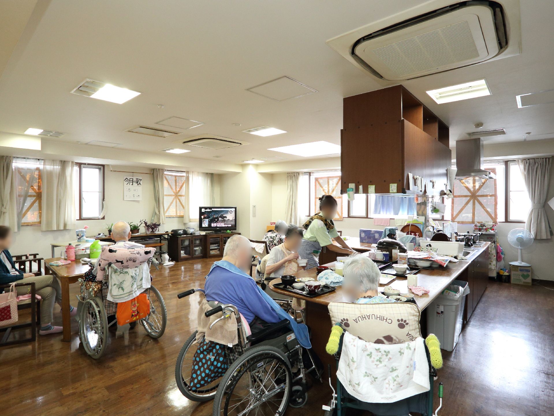 食事を食べている入居者様と、そのフォローをしているスタッフがいる。その横には、テレビを見ている入居者様もいる。