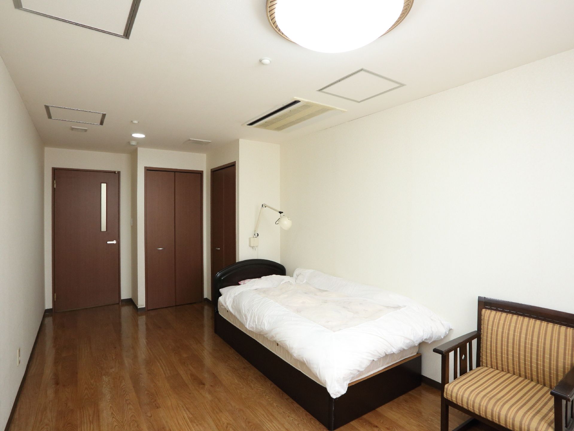 白色の天井と壁に木目仕様の床の内装である。壁際に介護用ベッドが置かれ、そばに1人掛けのソファが置いてある。