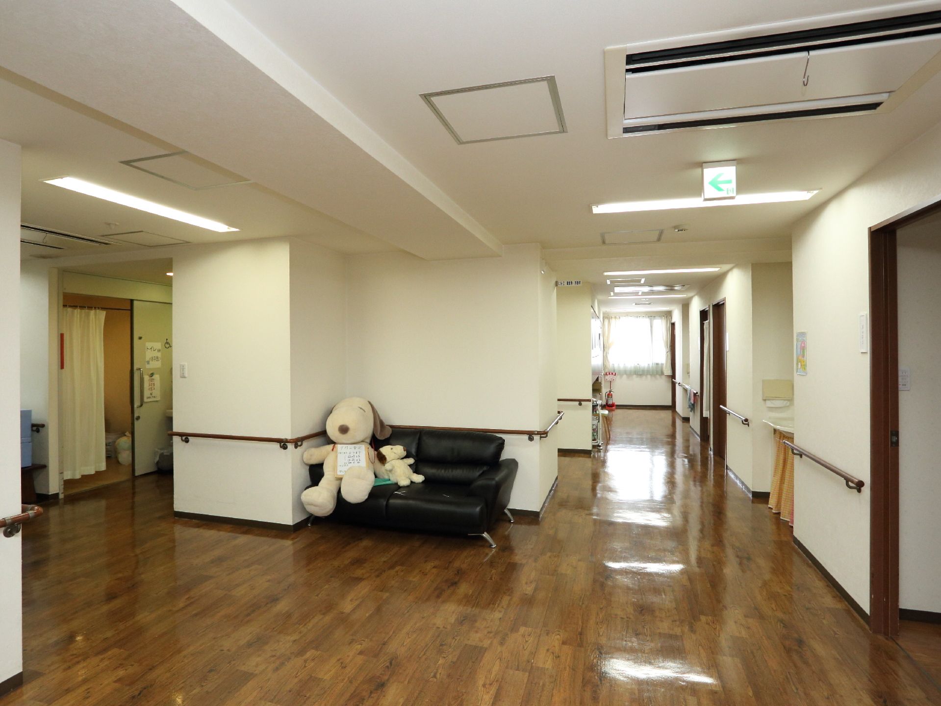 廊下の壁際には、黒いソファと大小のぬいぐるみが置かれてある。蛍光灯や非常口には電気がついて、明るくなっている。