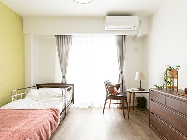 介護用ベッドとチェスト、丸机といすが置かれている広い個室