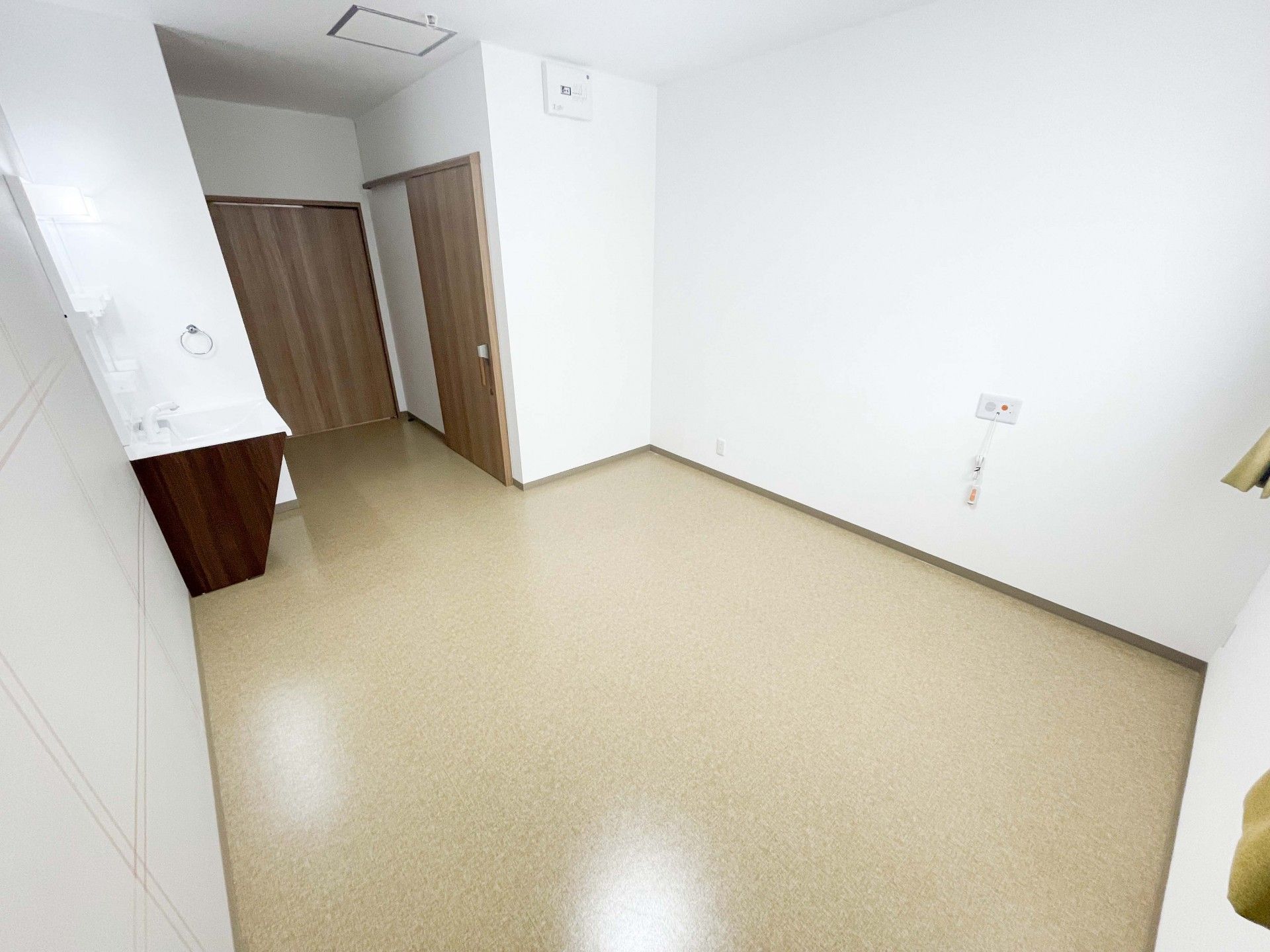 チェックの車いすに座った高齢女性を抱きかかえるようにして介助している若い女性スタッフ。スタッフはグリーンのエプロンを付けている。