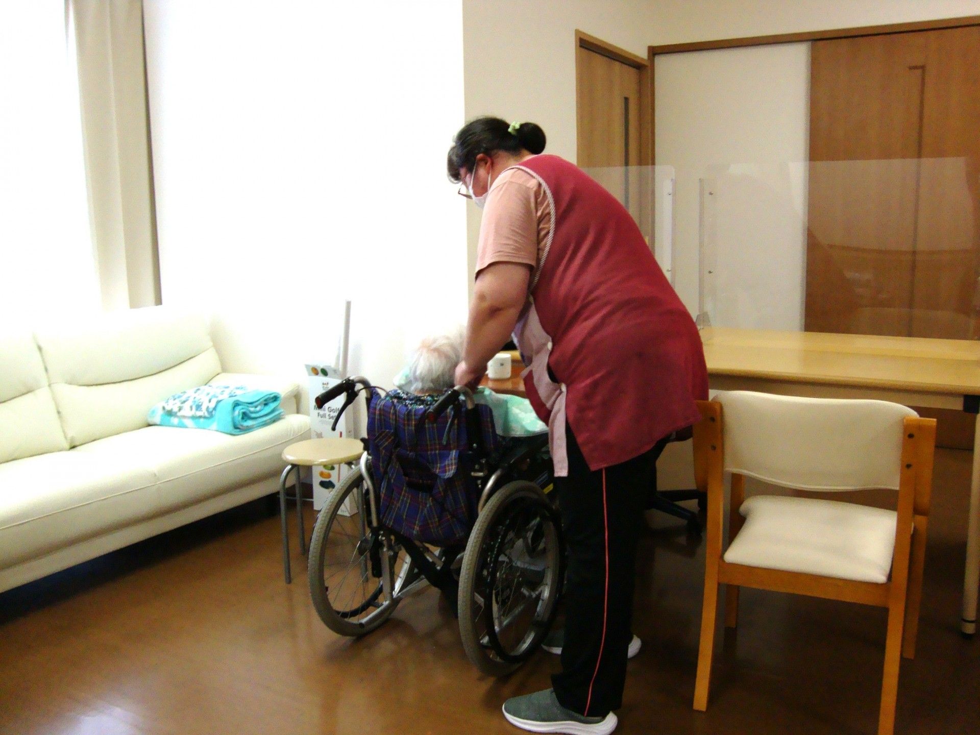 屋外で笑顔で過ごしている車いすの高齢女性と付き添いの高齢男性、男女のスタッフ。
