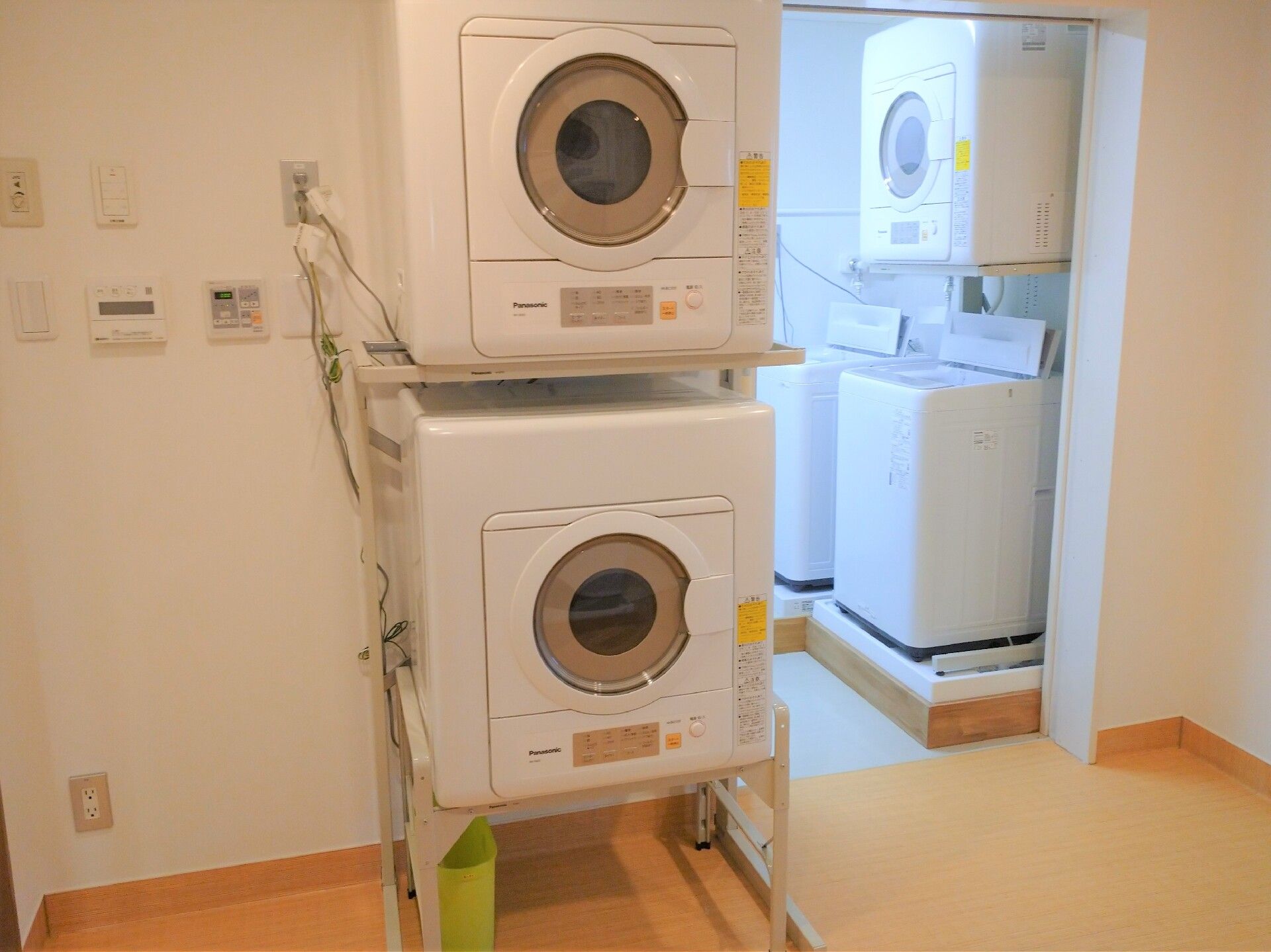 乾燥機と縦型の洗濯機が複数設置された洗濯室。奥の部屋には縦型の洗濯機と乾燥機があり、手前には乾燥機が設置されている。