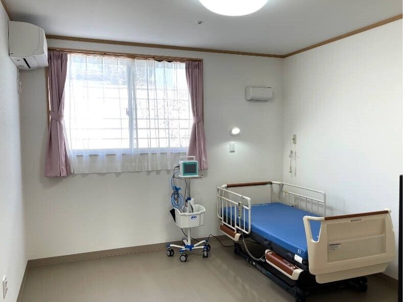 個室の部屋には介護ベッドがあり、ベッドサイドには緊急通報装置と医療器具が置かれている。