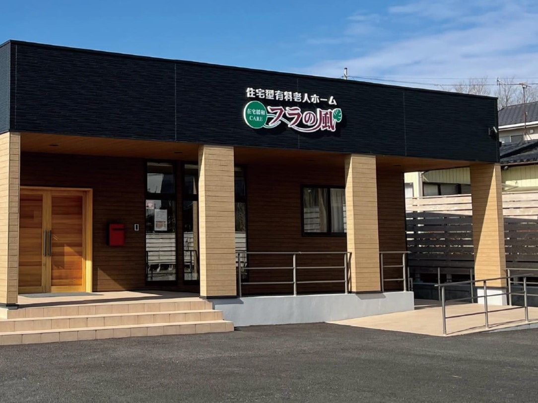 外壁にはホーム名が書かれ、平屋建ての建物は日当たり良好。玄関先には手すり付きのスロープと階段がある。