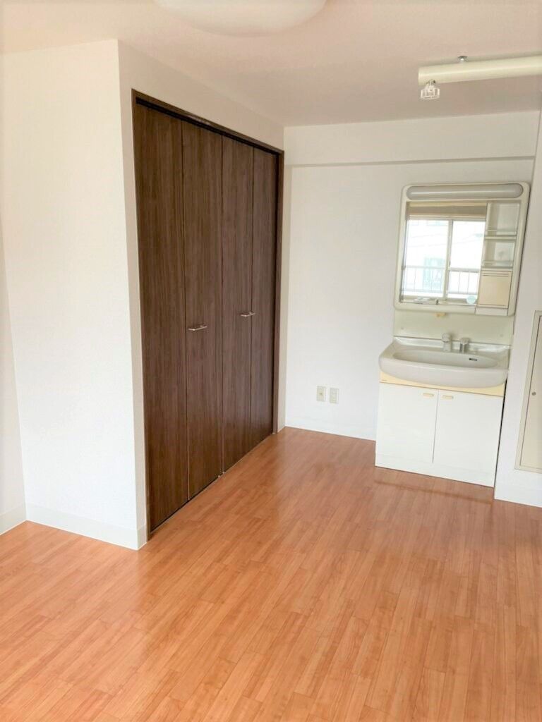 フローリングの部屋には大きなクローゼットが付いている。鏡が付いた洗面所があり、鏡にはカーテンが付いていない窓が映っている。