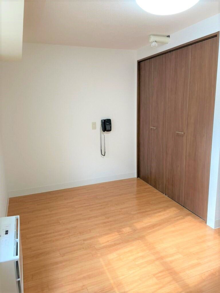 大きなブラウンの収納スペースがついたフローリングの部屋には家具や家電はなく、暖房器具が付き、日当たりも良好。電話のようなものがある。