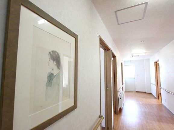 女性の絵が飾られた廊下にはパネルヒーターが設置され、窓があり明るい。