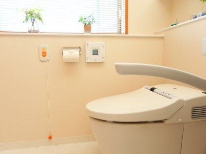 オレンジの呼び出しボタンや操作ボタンが壁に設置されたトイレ。手すりも付いている。