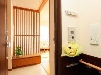 居室の出入り口にある手すりには黄色い花もある。居室内には観葉植物が飾られている。