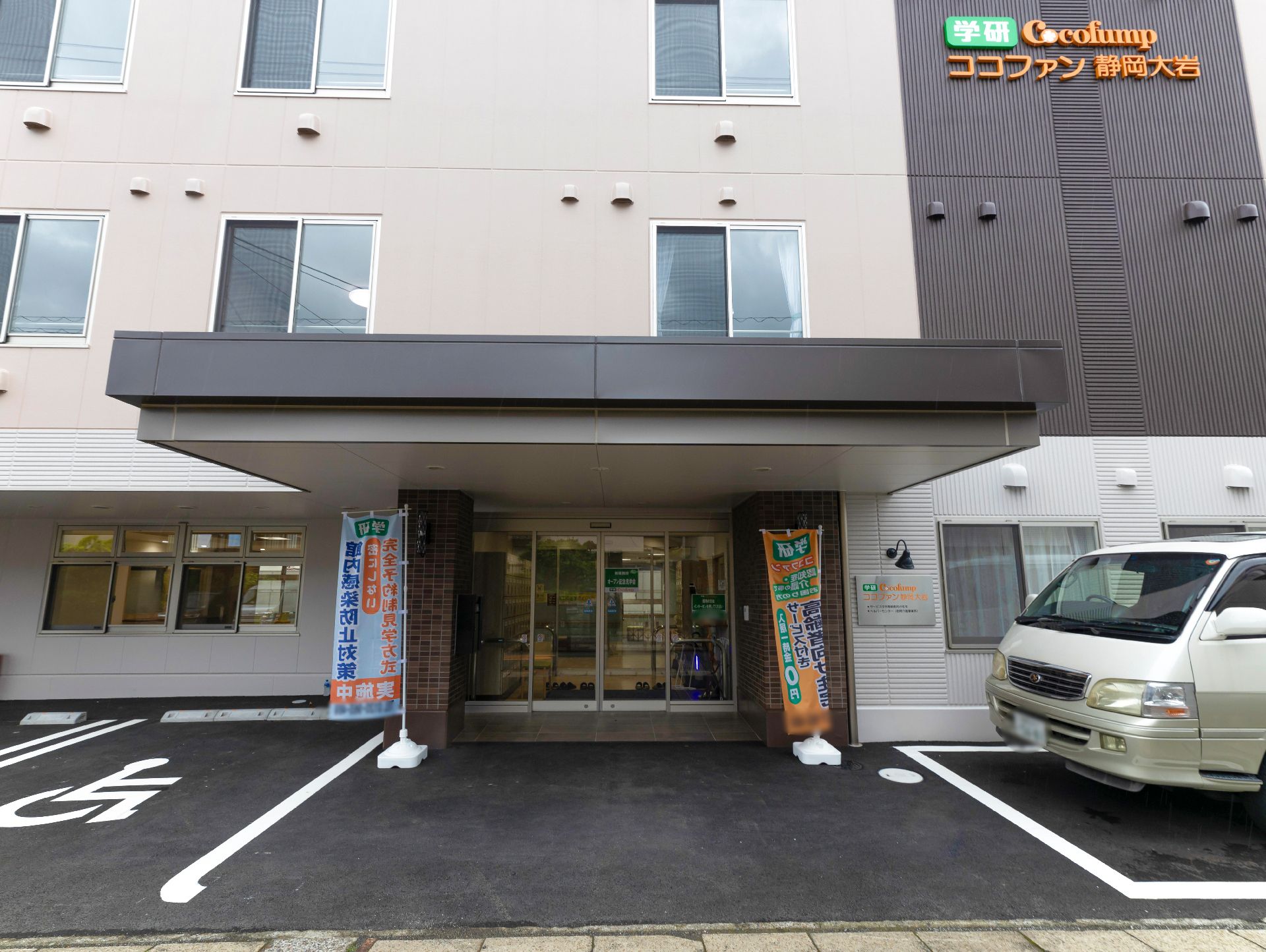 ブルーのエプロンを付けた若い女性スタッフが笑顔でブランのジャケットを着た高齢女性に付き添い、屋外を歩いている様子。周辺には原っぱが広がっている。