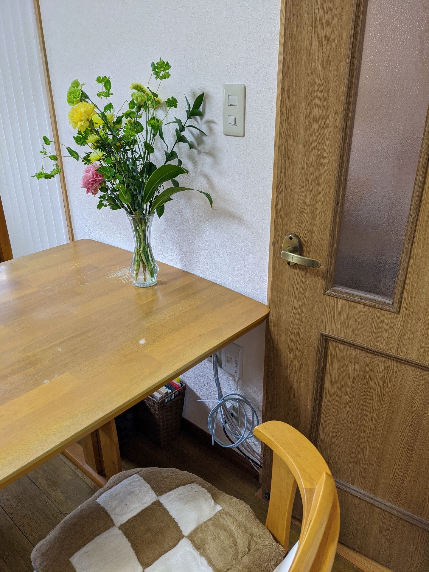 木製のダイニングテーブルの上に置かれた小さな透明のガラスの花瓶に黄色やピンク、白い花がきれいに活けられている。