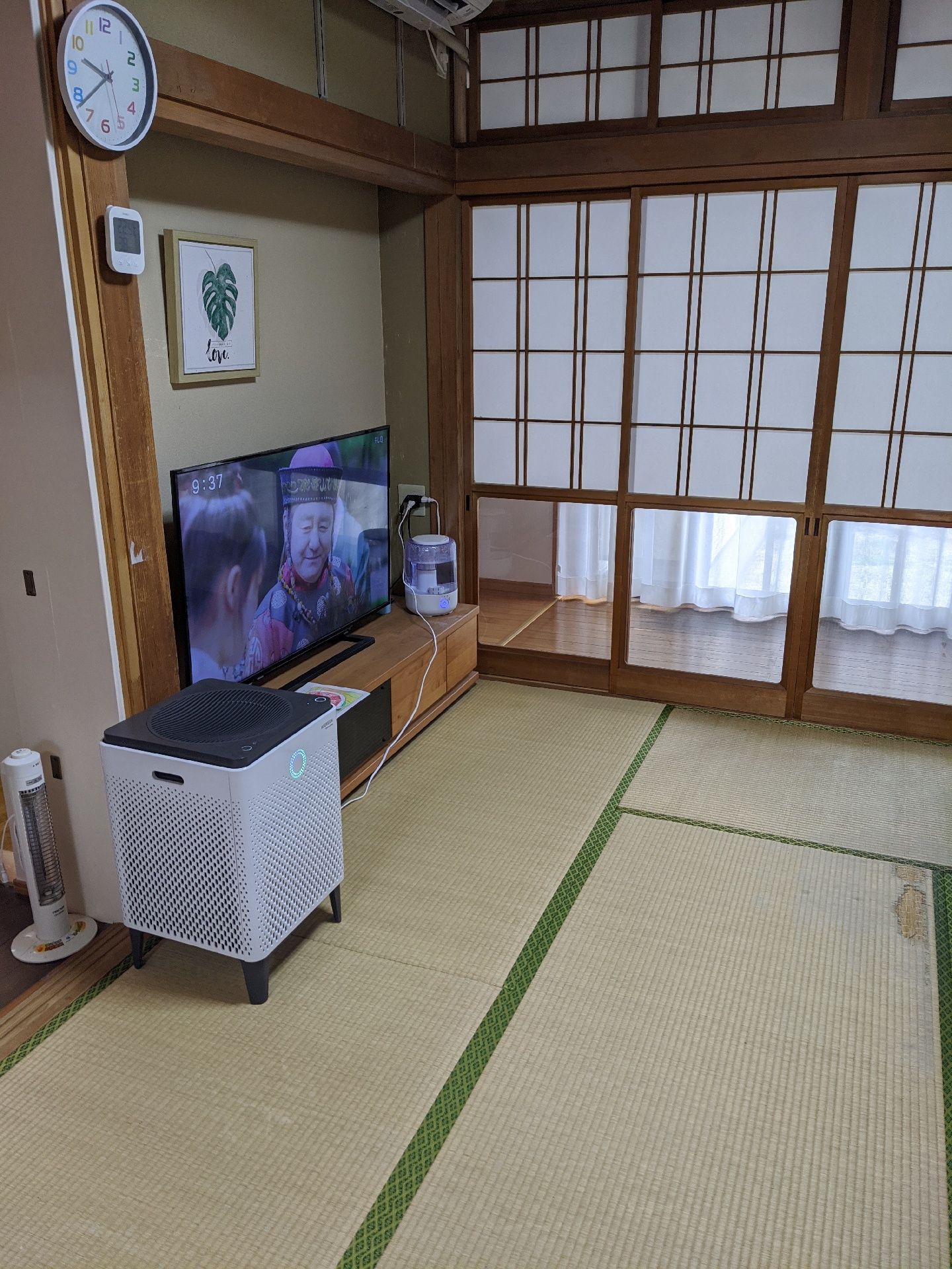 畳敷きの和室のリビングには空気清浄機や時計、テレビが置かれ、イラストも飾られている。一般の住宅のような雰囲気の場所。