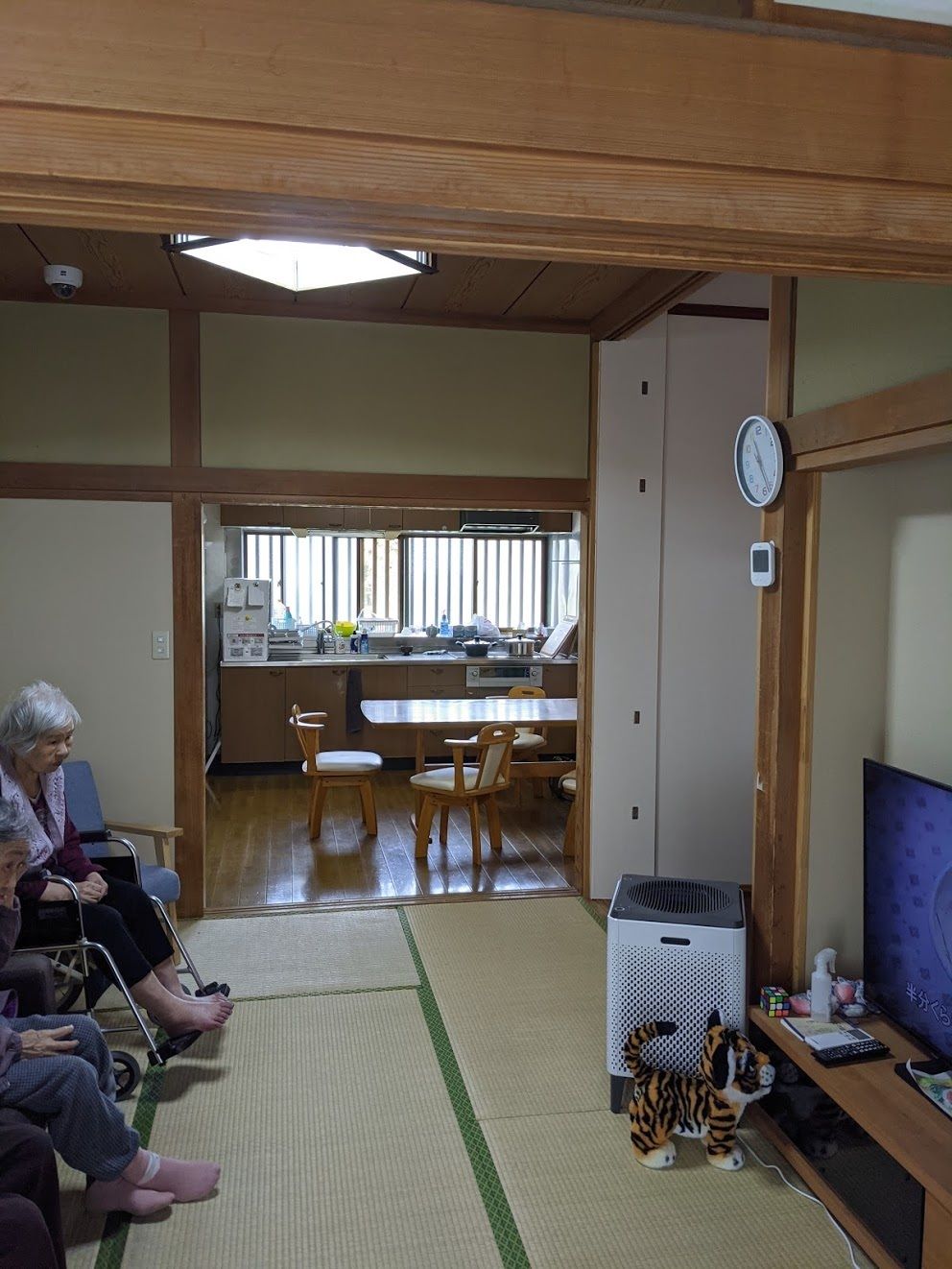 高齢者の方にタオルをかけてマッサージしているスタッフと振り返りながら会話する女性の様子