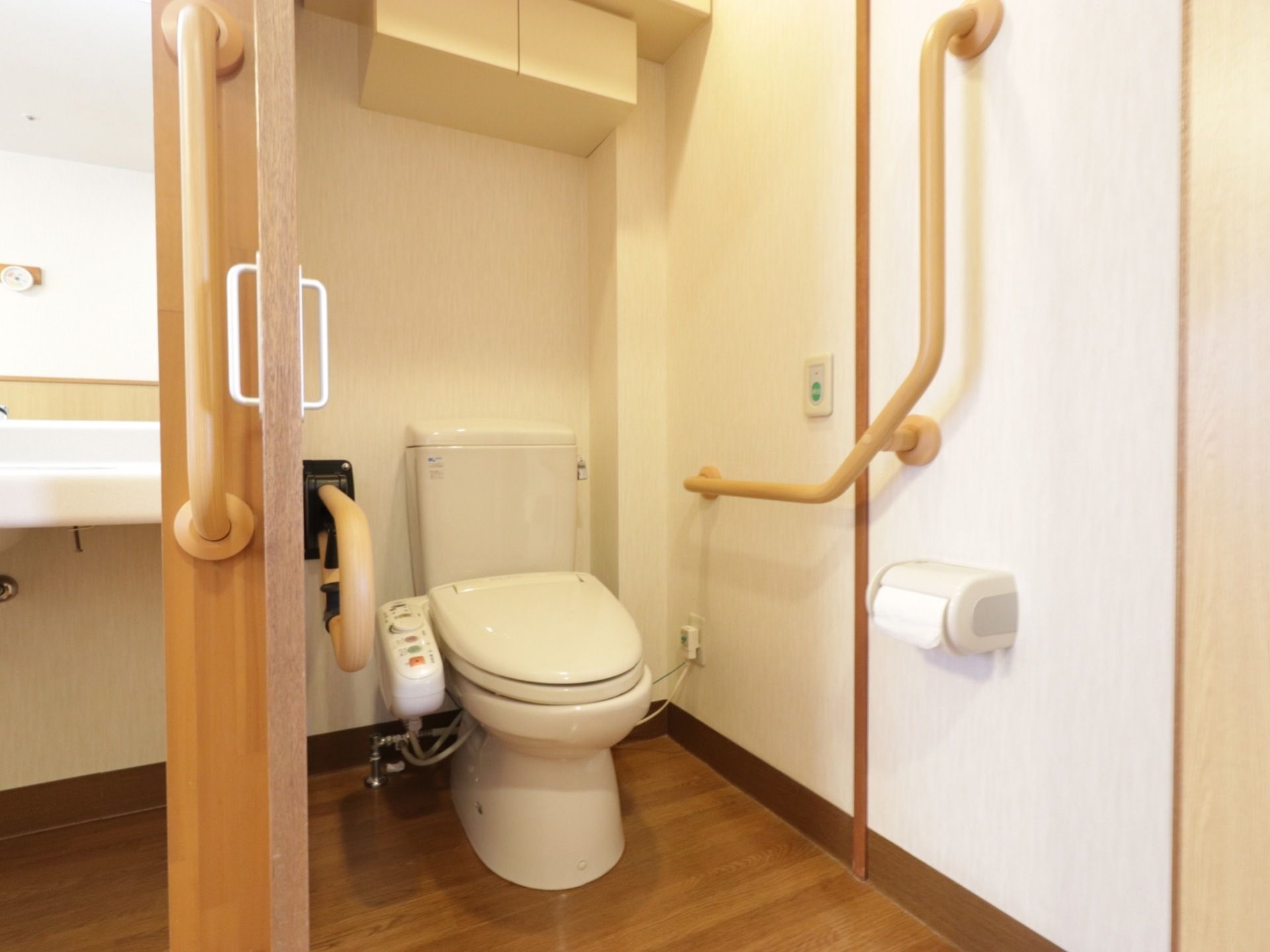 温水洗浄便座が付いたトイレは、出入り口に引き戸が取り付けられている。正面の壁の上の方に、ベージュ色の収納スペースがある。