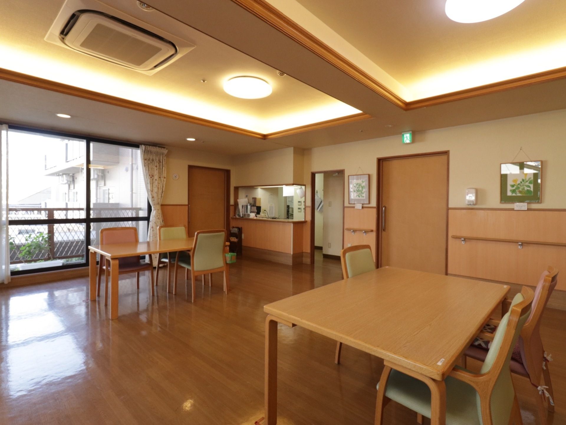 木目調デザインの床は、段差の無いバリアフリーである。奥の壁には、緑色の枠で囲まれた黄色い花の絵が掛けてある。
