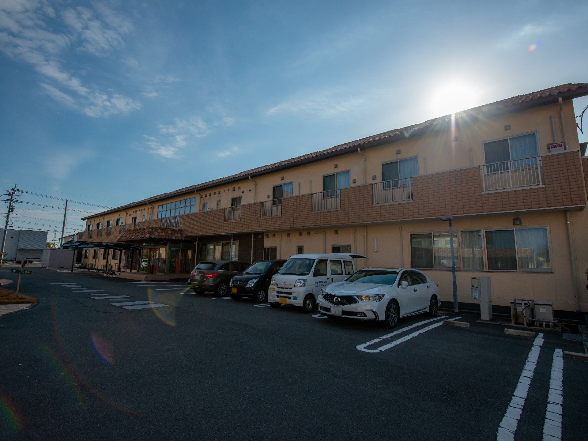 ブルーのエプロンを付けた若い女性スタッフが車いすの高齢女性に付き添っている。女性は誰かに向かって手を振っている。