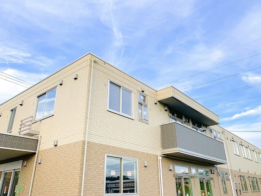 ２階建ての建物は日当たり良好でベージュ系の色合い。ベランダも付いている。