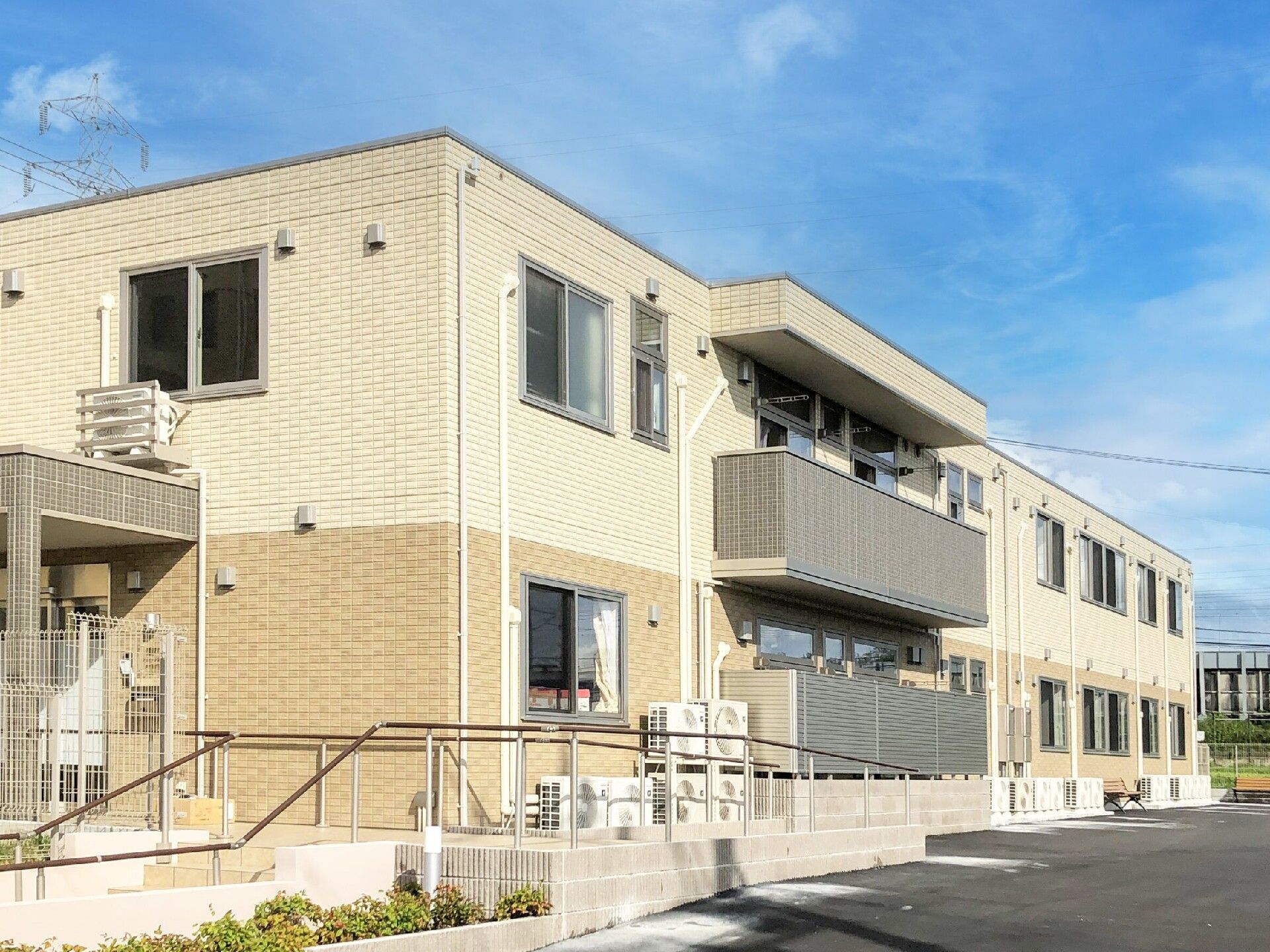 ベージュ系の２階建ての建物は日当たりのいい場所に建っている。玄関には手すり付きのスロープが設置されている。