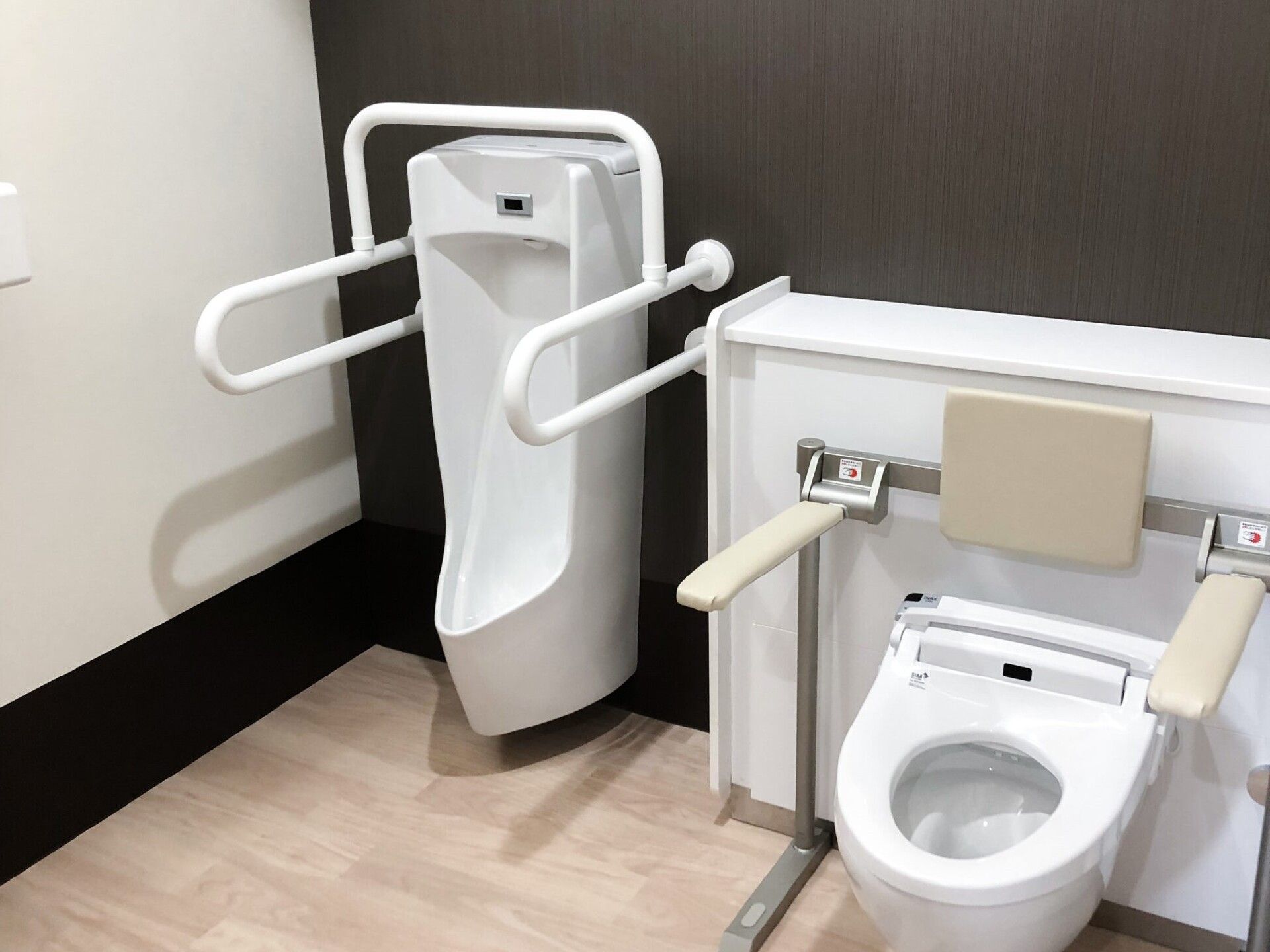 男性用の小便器や手すりや背もたれ付きの便座が設置されている広いトイレ。