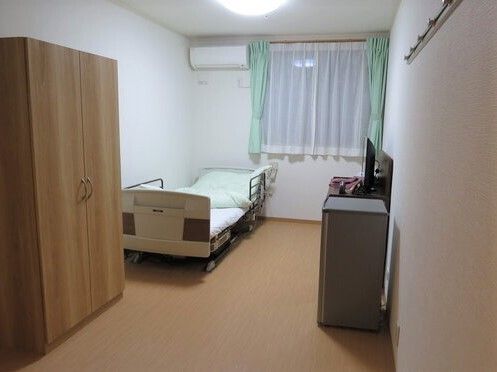 大きなクローゼットやエアコン、寝具付きのベッドが設置された居室。タンスの上にはテレビもあり、窓にはカーテンとレースカーテンが付いている。