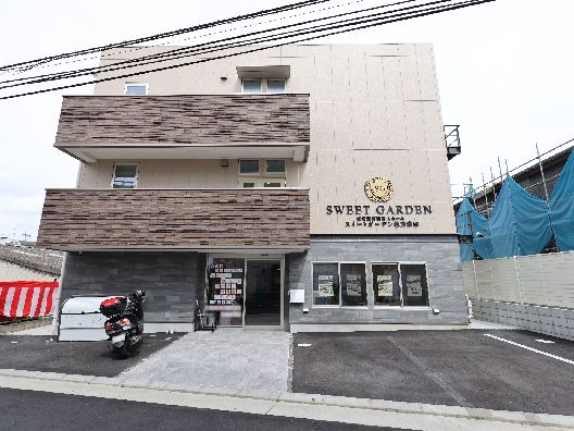 カーディガンを着た高齢女性とエプロンを付けた女性スタッフが隣同士に立ち、体を寄せ合っている。