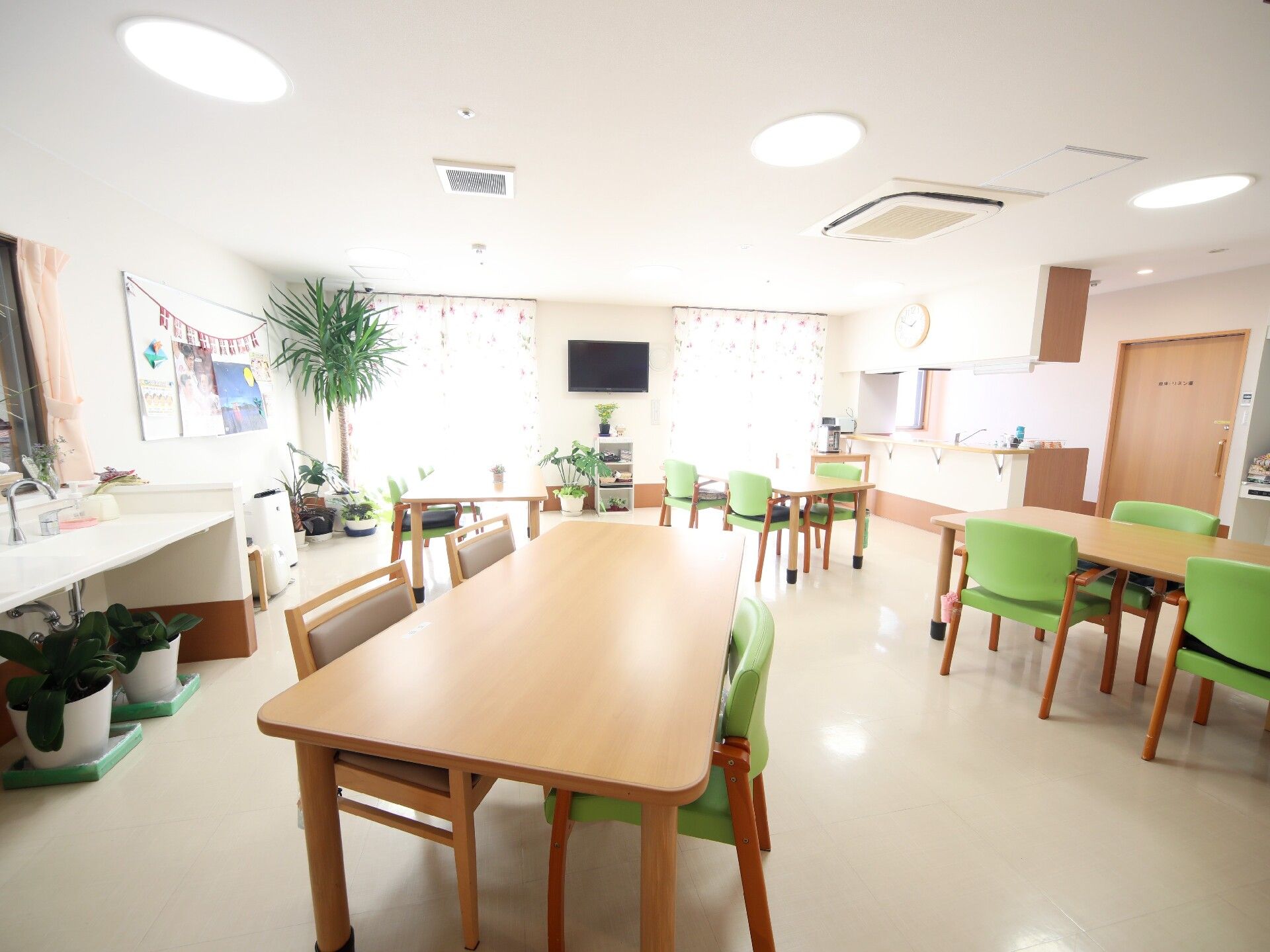 グリーンの椅子がセットされたダイイングテーブルが複数並んだスペースには車いす対応の洗面所があり、テレビも付いている。
