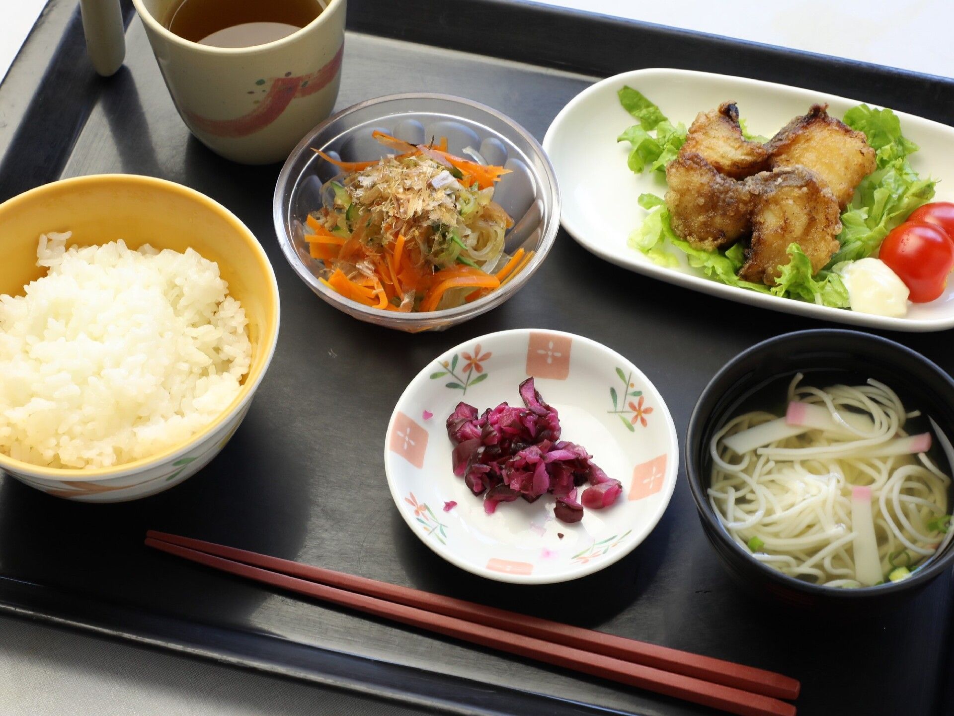 魚の竜田揚げには生野菜が添えられ、シバ漬けやそうめん入りの汁物、野菜の和え物などが並べられ、白いご飯もある。