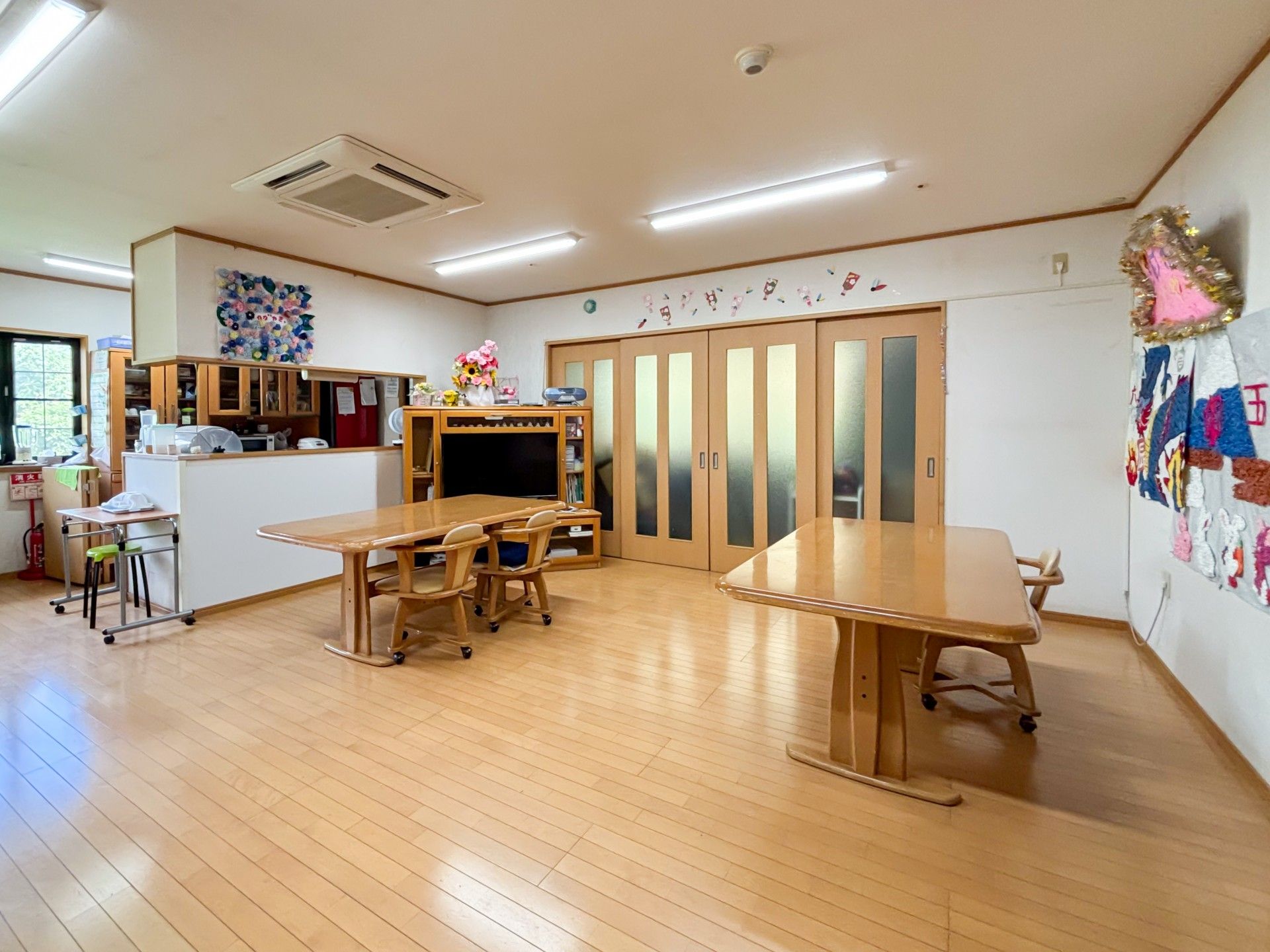 屋外で笑顔で過ごす車いすの高齢女性と付き添いの高齢男性。男女のスタッフも周りにいる。