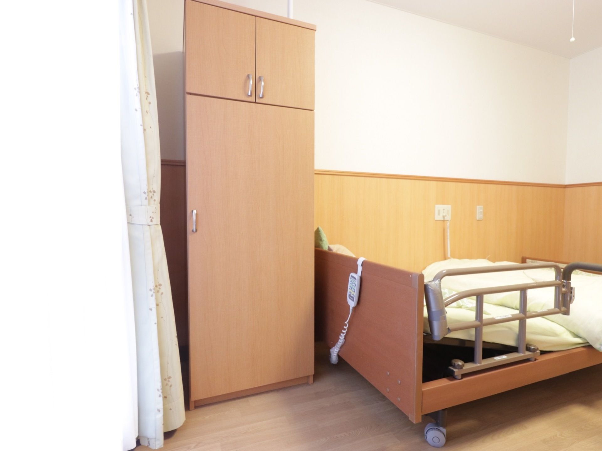 居室の窓とベッドに挟まれるようにして縦長のクローゼットが置いてある。扉は２段あり、縦長の下の段は衣類の収納用のようだ。