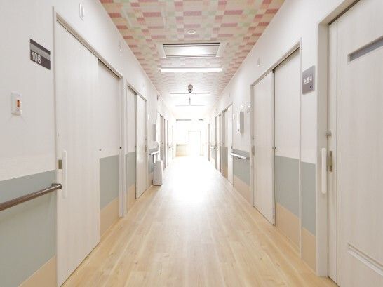 白を基調とした館内。廊下はフローリングで日当たりがよく、ブラウンの手すりが両サイドに付き、壁はグレーと白の2食使いで居室のドアは真っ白。