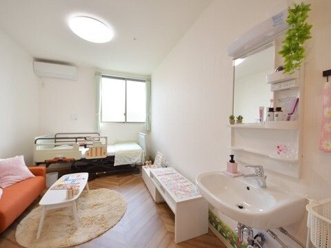 エアコンが付いたフローリングの部屋。窓際には寝具がセットされた介護ベッドが置かれ、ソファやラグ、テーブルなどもあり、洗面所も付いている。