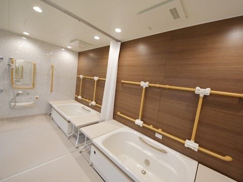 手すりがたくさんついた安全性の高い浴室。二つの浴槽のサイドにはベンチがあり、浴槽の間にはカーテンが付いている。呼び出しボタンやシャワーもある。